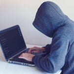 anonymous hacker with on laptop in white room